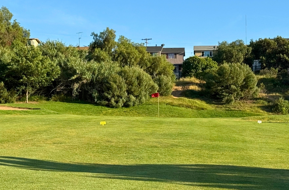 Golf green with red flag and yardage markers at National City Golf Course, residential backdrop